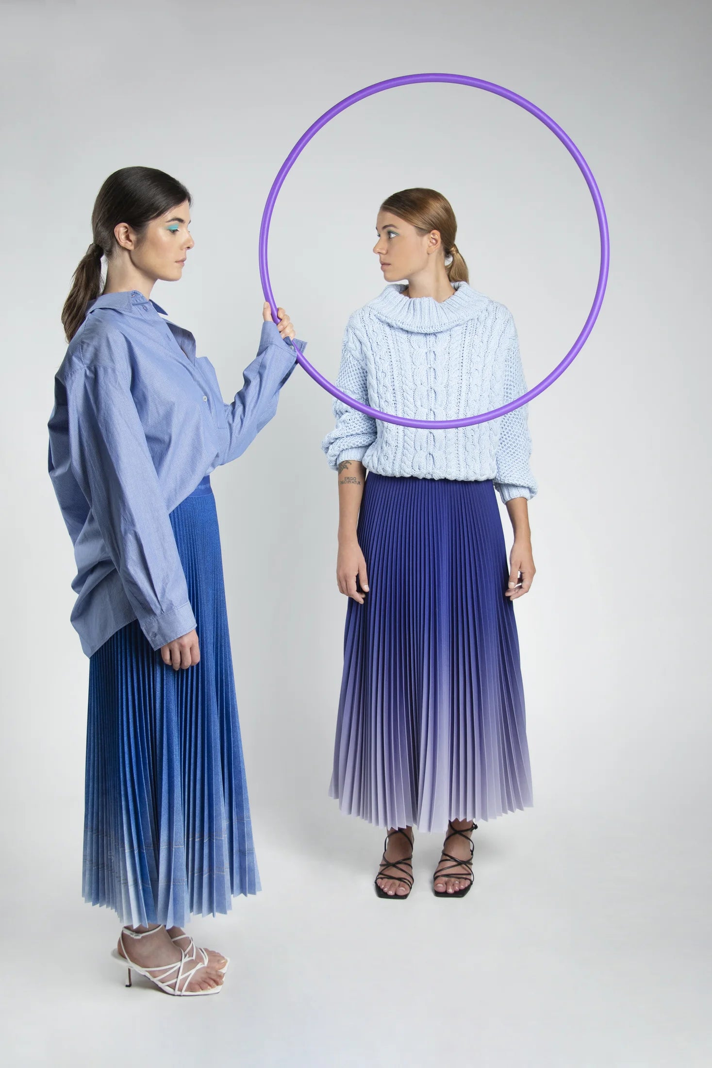 Two women wearing blue Stylyne pleated skirts in an art studio photograph