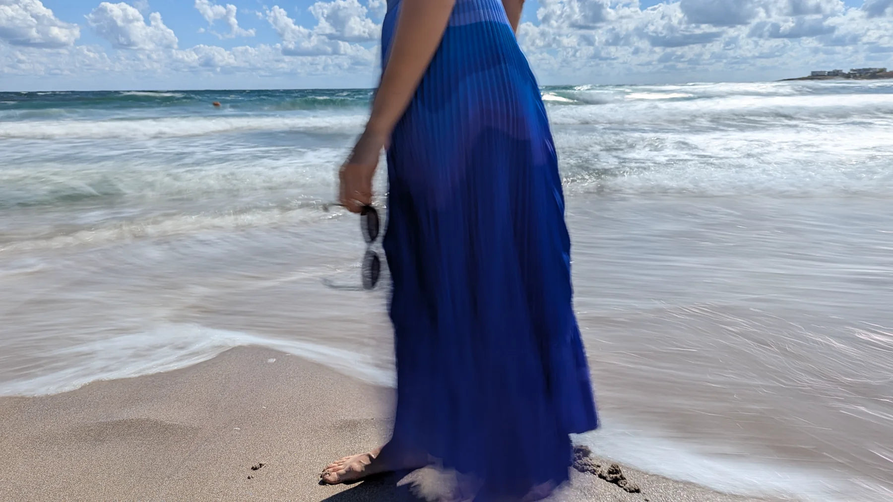 Nadya, founder of Stylyne, walking beside the sea in a blue pleated skirt