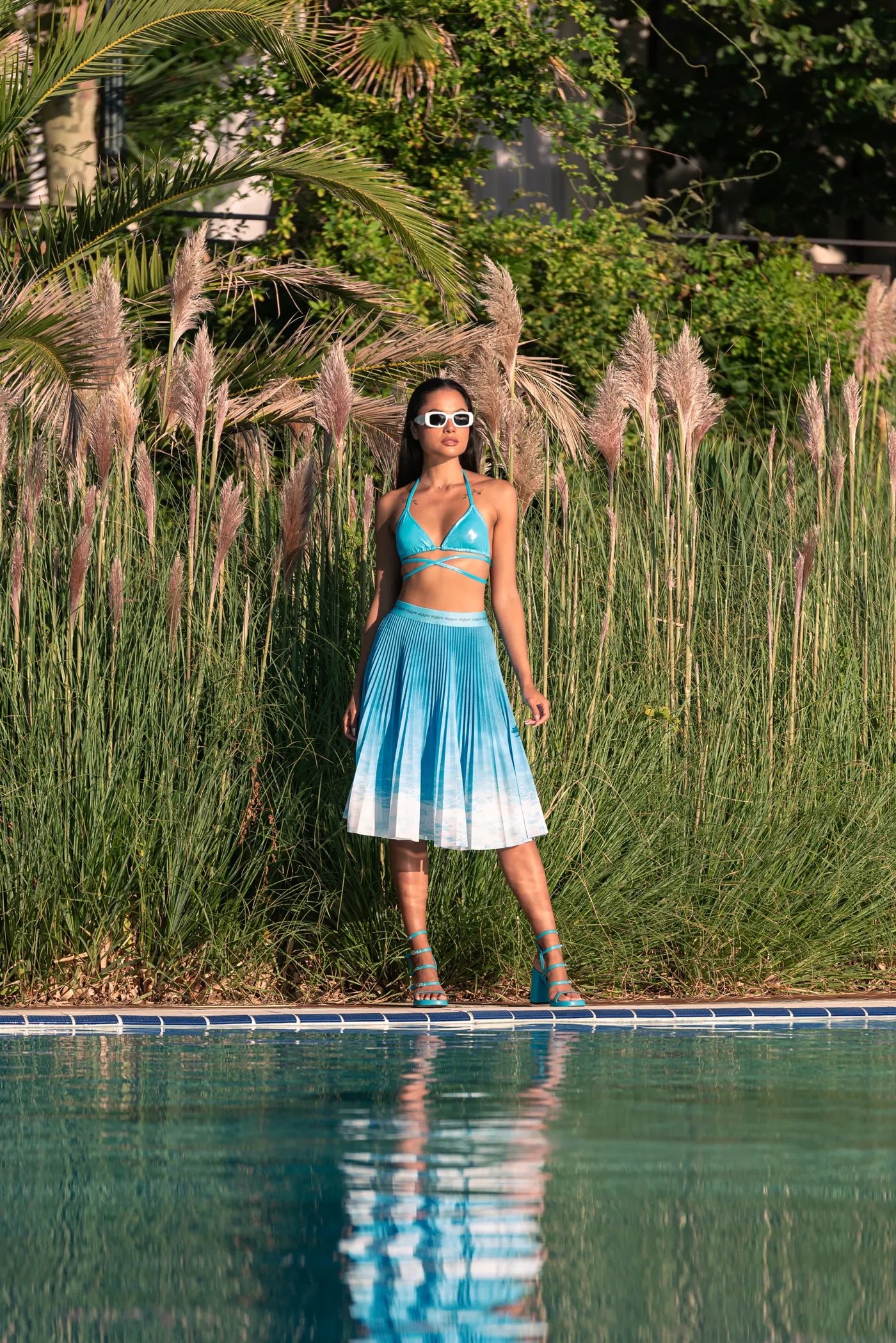 A woman wearing a blue Stylyne pleated skirt beside a pool
