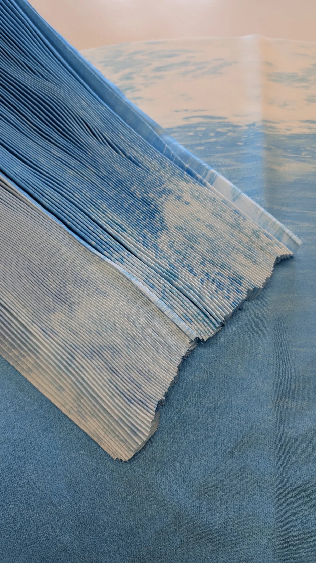 Blue printed fabric shown flat beneath a precisely pleated section